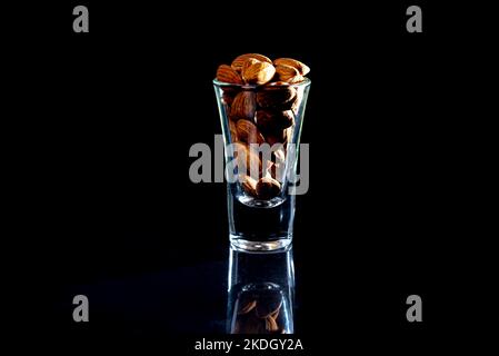Peeled almond in jar glass bucket on a black isolated background. Row of bowls with almond nuts, front view. Peeled almond pattern Stock Photo