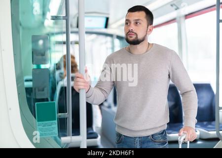 Young bearded man with suitcase riding in streetcar Stock Photo