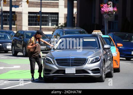 Toronto, Canada - August 12, 2022: Squeegee man wipes windshield of Mercedes-Benz in traffic. Stock Photo