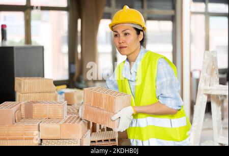 Female builder is laying bricks on top of each other Stock Photo