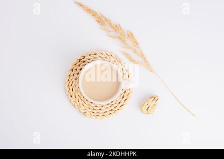 Coffee or cocoa cup on a wicker coaster and pampas grass on white background. Still life. Top view, flat lay. Stock Photo