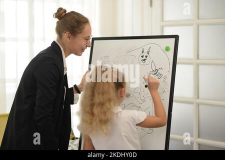 A  teacher teaches her young daughter to paint with colorful pens in the school classroom. concept of child rearing education By being a creative and Stock Photo