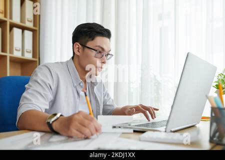Young architect reading e-mail from client and taking notes in planner Stock Photo
