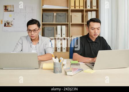 Concentrated young engineers working on laptops at office table in bureau Stock Photo