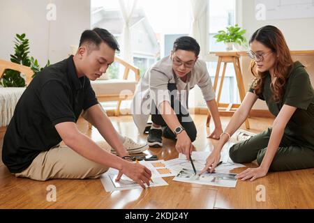 Team of young architects working with photos and blueprints when sitting on wooden floor in home office Stock Photo