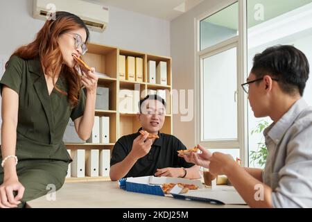 Group of colleagues eating pizza for lunch at office table Stock Photo