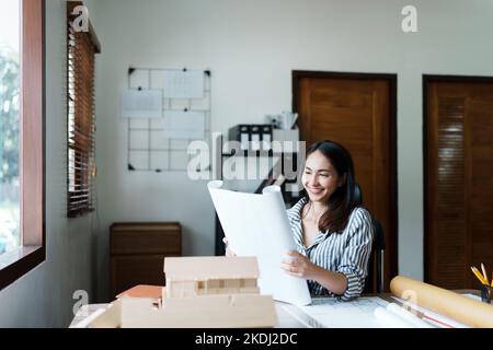 Portrait of an Asian female engineers are designing house structures and architectural using blueprints, rulers, pencils, dividers and building models Stock Photo