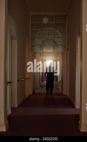If these walls could talk...Rearview shot of an unidentifiable senior woman walking down a hallway with her walking stick. Stock Photo