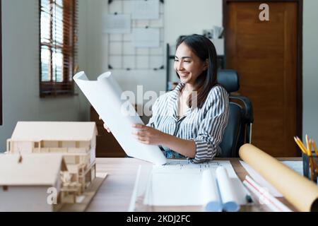 Portrait of an Asian female engineers are designing house structures and architectural using blueprints, rulers, pencils, dividers and building models Stock Photo