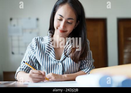 Portrait of an Asian female engineers are designing house structures and architectural using blueprints, rulers, pencils, dividers and building models Stock Photo
