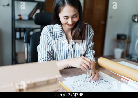 Portrait of an Asian female engineers are designing house structures and architectural using blueprints, rulers, pencils, dividers and building models Stock Photo