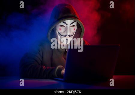 June 5, 2022 Novosibirsk, Russia: Anonymous in a hood is typing on a laptop in the dark in red-blue smoke.  Stock Photo
