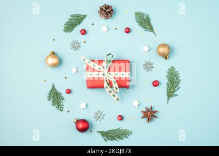 Christmas or Happy New Year gift box in frame made of fir tree branches, holiday decorations on blue background. Flat lay. Top view with copy space Stock Photo