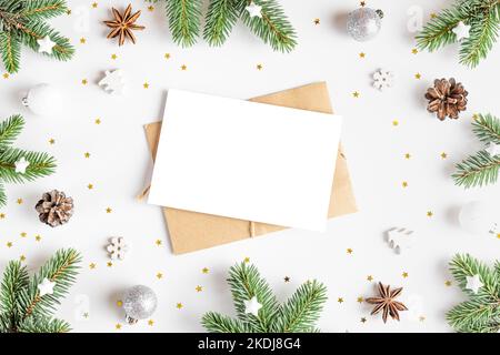 Christmas greeting card in frame made of fir tree, holiday decorations on white background. Mock up. Flat lay. Top view Stock Photo