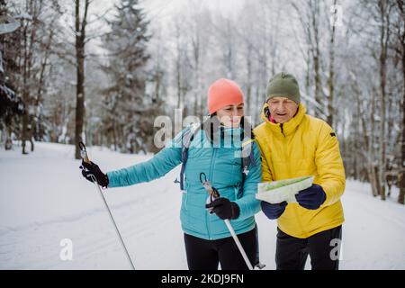 Senior couple looking at paper map during cross country skiing in snowy forest. Stock Photo