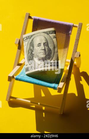 Rolled bill on deck chair, flip-flops, sand and piggy bank on white ...