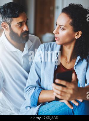 Whos number is this. a dismayed couple receiving bad news via a smartphone at home. Stock Photo