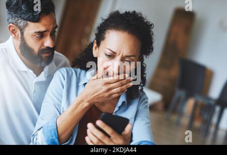 How could this happen. a dismayed couple receiving bad news via a smartphone at home. Stock Photo