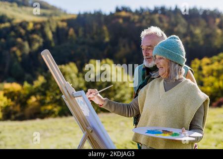 Senior couple painting together in nature, during autumn day. Stock Photo