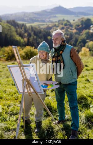 Senior couple painting together in nature, during autumn day. Stock Photo