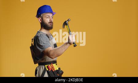 Construction worker using manual hammer to hit nails in wall, working with sledgehammer or mallet to break and wreck. Handyman doing rebuilding work with mechanical instrument and tools. Stock Photo