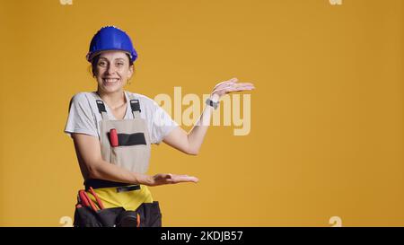 Portrait of construction worker advertising sideways space, pointing left or right to show message in studio. Indicating sides direction to do advertisement. Woman with refurbishment work. Stock Photo
