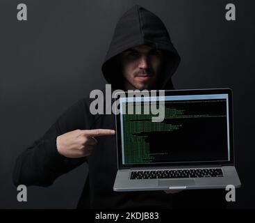 How secure is your laptop really. Portrait of an unidentifiable computer hacker holding up a laptop against a dark background. Stock Photo