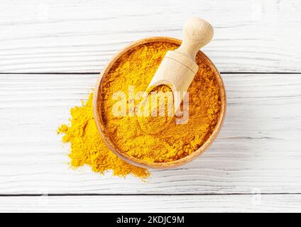 Dry turmeric (curcuma) powder in wooden bowl with scoop on white wooden background Stock Photo