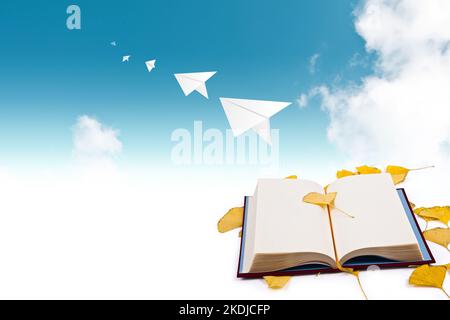 A paper airplane is flying (flying) to the sky with ginkgo leaves and books on the background, golden ginkgo leaves in autumn are placed. The backgrou Stock Photo
