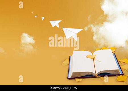 A paper airplane is flying (flying) to the sky with ginkgo leaves and books on the background, golden ginkgo leaves in autumn are placed. The backgrou Stock Photo