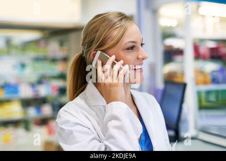 Yes, we do deliver. a young pharmacist talking on a cellphone in a chemist. Stock Photo
