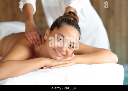 Happy woman receiving a massage in the back in spa looking at camera Stock Photo
