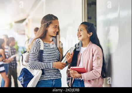 How did you do on the test. two happy schoolgirls chatting in the hallway outside their classroom. Stock Photo