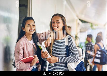 Were too cool for school. Portrait of two happy schoolgirls standing together in the hallway outside their classroom. Stock Photo