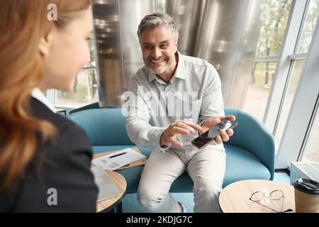 Smiling man showing funny photos on phone to female colleague Stock Photo