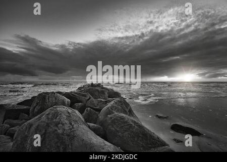 Sunset on the beach in Denmark taken in black and white. Stone groyne in the foreground. Walk on the coast in the sand. Landscape photo by the sea Stock Photo