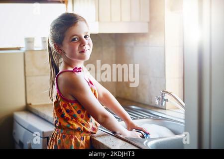 I dont mind helping with the housework. Portrait of a little girl washing dishes at home. Stock Photo