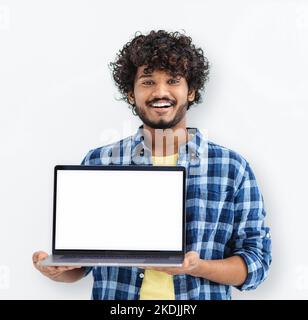 Happy Indian man student standing with open laptop with blank white mockup screen on white background Stock Photo