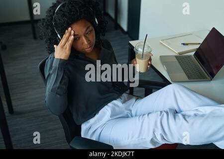 Woman sitting in an office chair and holding her head Stock Photo