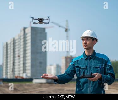 A man in a helmet and overalls controls a drone at a construction site. The builder carries out technical oversight. Stock Photo