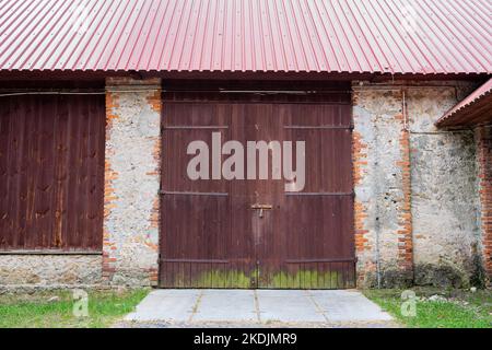 The door to an old brick barn covered with a corrugated metal roof Stock Photo