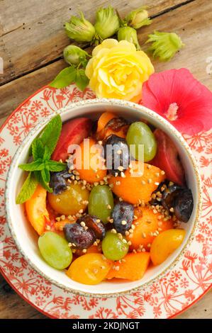 Summer fruit salad with melon, grapes, plums, peaches, mint, buckwheat seeds, hazelnuts, edible hollyhock flower and rose Stock Photo