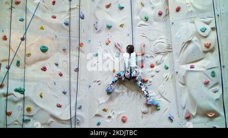 child climbs on a special wall for mountaineering. the girl of seven years in safety equipment is engaged in rock climbing on a special training vertical wall,. High quality photo Stock Photo