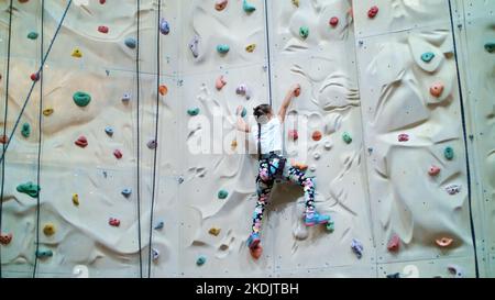 child climbs on a special wall for mountaineering. the girl of seven years in safety equipment is engaged in rock climbing on a special training vertical wall,. High quality photo Stock Photo