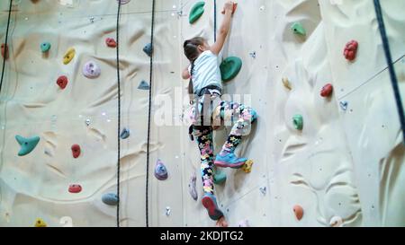 child climbs on a special wall for mountaineering. the girl of seven years in safety equipment is engaged in rock climbing on a special training vertical wall,. High quality photo Stock Photo