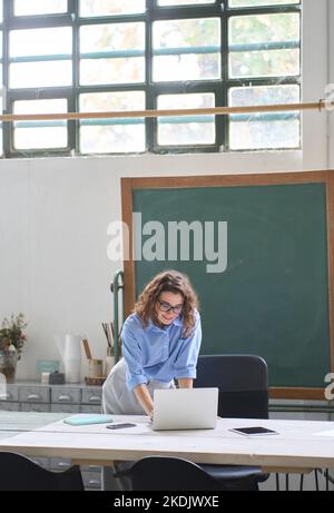 Young woman school teacher or employee standing at desk using laptop. Stock Photo