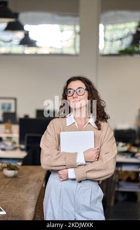 Young dreamy professional business woman standing in modern office thinking. Stock Photo