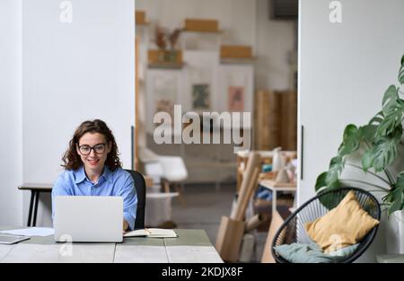 Young smiling business woman or student sitting at desk using laptop.