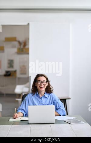 Young cheerful business woman student sitting at office desk with laptop. Stock Photo