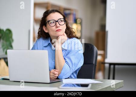 Thoughtful serious professional woman using laptop, looking away thinking. Stock Photo